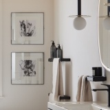 lifestyle image of vado cameo muse 300mm black glass shelf insert and black shelf frame in bathroom for bottles with towel hanging beside MUS-085-30-BLK and MUS-184-60-MB